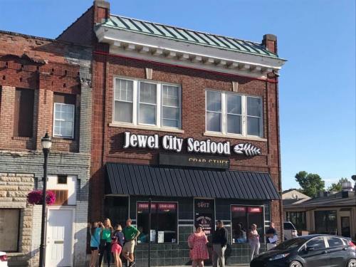 Exterior of Jewel City Seafood, a brick building with a sign, and people gathered outside on a sunny day.