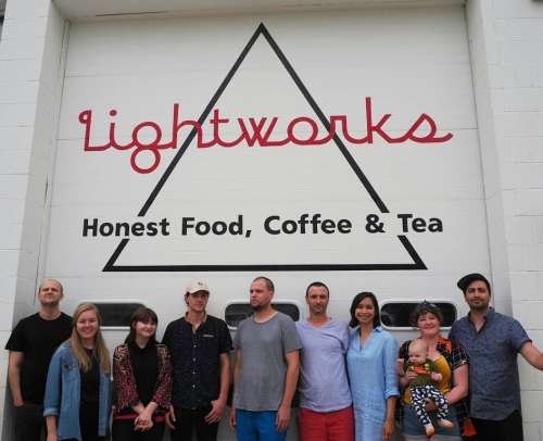 A group of diverse people stands in front of a sign that reads "Lightworks: Honest Food, Coffee & Tea."