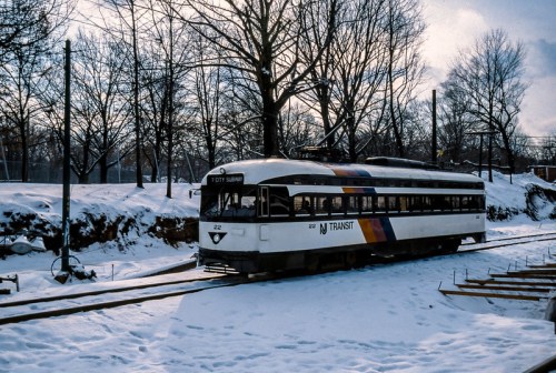 A NJ Transit train on snowy tracks, surrounded by bare trees and a winter landscape.