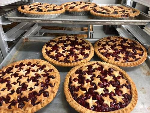 A tray of freshly baked fruit pies with star-shaped crusts, arranged in a bakery setting.