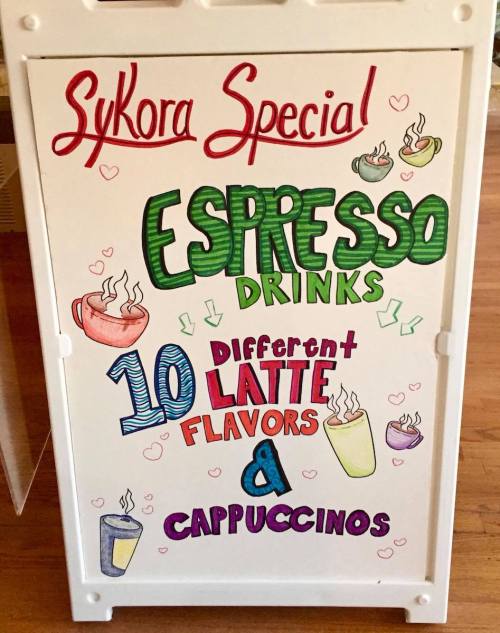 A sign promoting "Sykora Special" espresso drinks with 10 latte flavors and cappuccinos, decorated with colorful drawings.