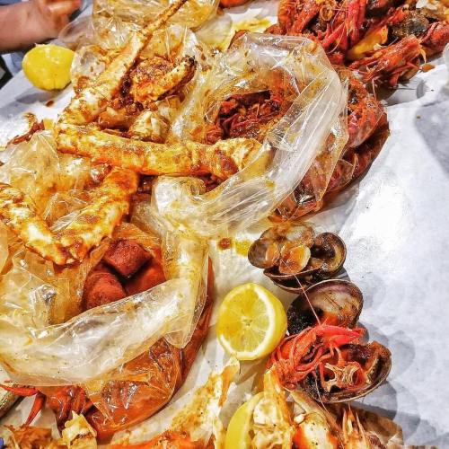 A spread of seafood including crabs, shrimp, and clams, served with lemon wedges on a table covered in plastic.