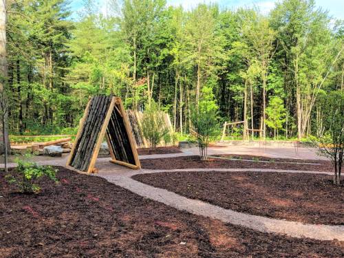 A serene outdoor space with wooden structures, pathways, and lush greenery in a forested area.