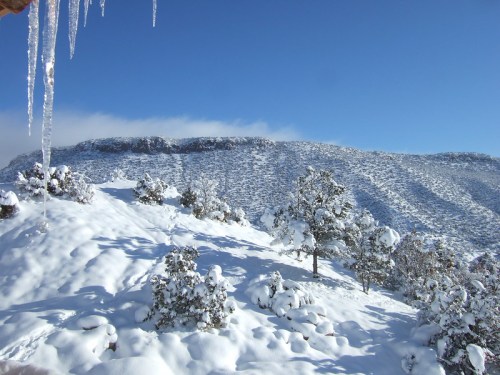 A snowy landscape with icicles hanging, featuring a mountain in the background under a clear blue sky.