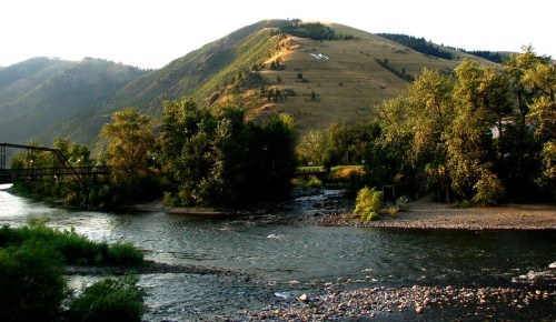 A serene river flows through a lush landscape, with rolling hills and trees under a clear sky.