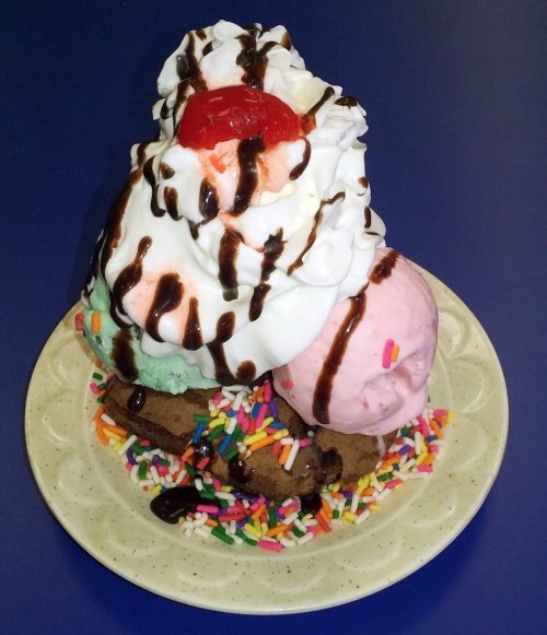 A colorful ice cream sundae with three scoops, whipped cream, a cherry on top, and sprinkles on a plate.