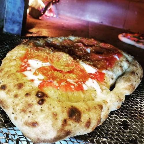 A freshly baked pizza with pepperoni and melted cheese, resting on a wire rack in a wood-fired oven.
