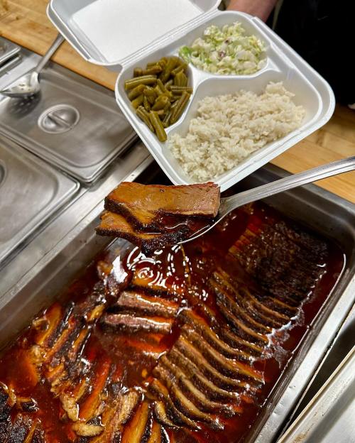 A spoonful of beef brisket in sauce, with a side of green beans and rice in a takeout container.