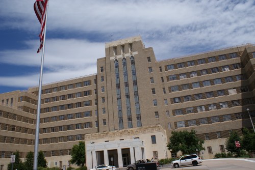 Historic building with a tall, textured facade, flagpole in front, under a partly cloudy sky.