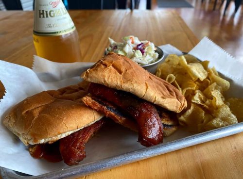 Two BBQ sandwiches on a tray with chips and coleslaw, alongside a bottle of beer.