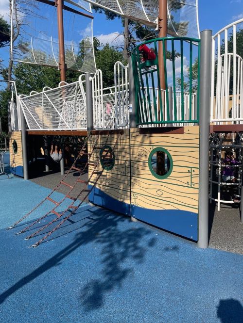 A colorful playground structure with climbing ropes, slides, and play areas surrounded by rubber flooring.