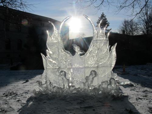 A large ice sculpture resembling flames, illuminated by sunlight, set against a snowy landscape.