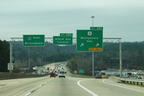 Highway exit signs for Birmingham and Montgomery, with traffic lanes visible under a cloudy sky.