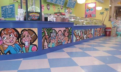 Colorful ice cream shop interior featuring vibrant murals of people enjoying ice cream, with a blue and pink checkered floor.