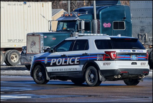 A police SUV from Clinton parked near a large truck in an industrial area.