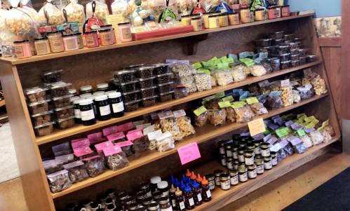 A wooden shelf filled with jars and containers of various snacks, candies, and preserves, labeled with colorful tags.