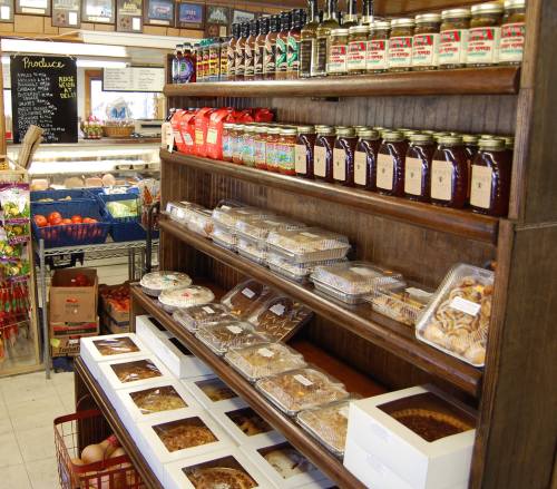 A wooden shelf filled with jars, baked goods, and produce in a cozy market setting.