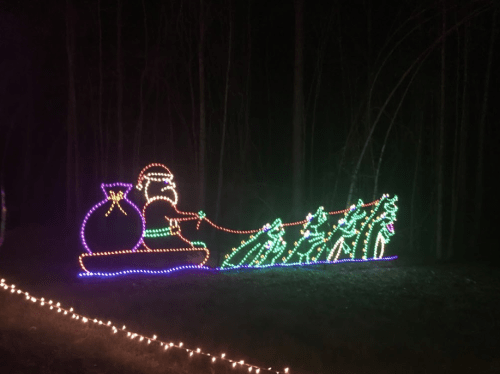 Colorful Christmas lights depict Santa in a sleigh, pulling a line of decorated trees against a dark background.