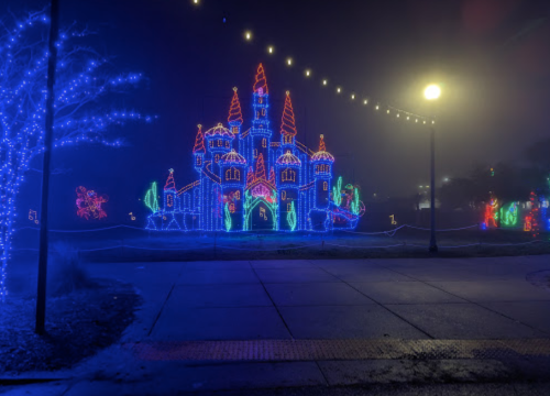 A brightly lit castle made of colorful Christmas lights, surrounded by fog and festive decorations.