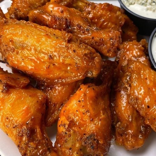 A plate of crispy, golden-brown chicken wings with a side of dipping sauce.