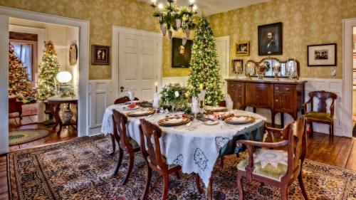 A festive dining room with a decorated table, Christmas trees, and warm lighting, creating a cozy holiday atmosphere.