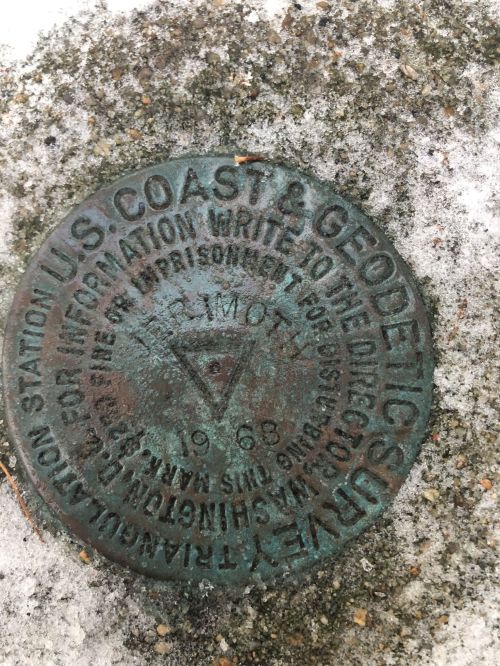 A weathered metal survey marker from the U.S. Coast & Geodetic Survey, dated 1963, embedded in a snowy surface.