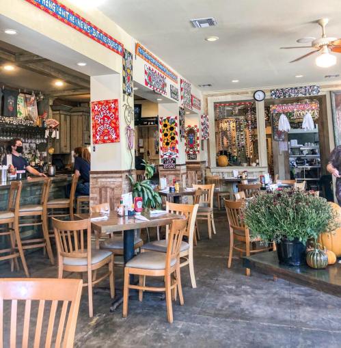 A vibrant restaurant interior with wooden tables, chairs, and colorful wall decorations. Staff are seen in the background.