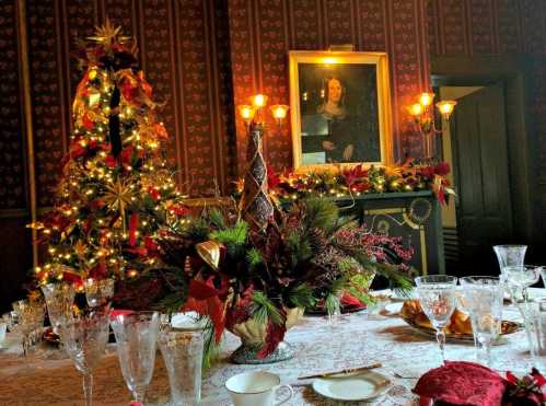 A festive dining table set with crystal glassware, surrounded by a decorated Christmas tree and holiday decor.