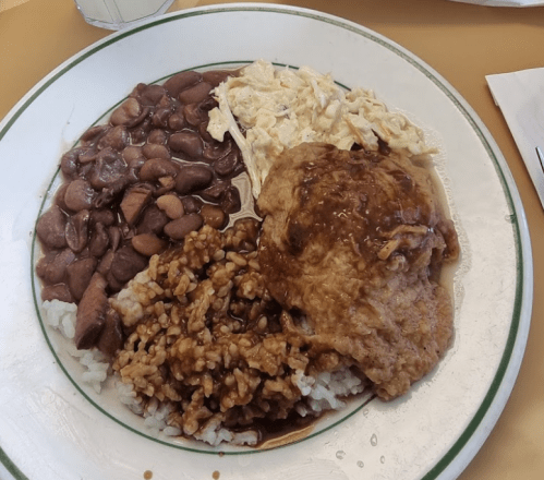 A plate of food featuring rice, beans, shredded chicken, and a piece of meat with gravy.