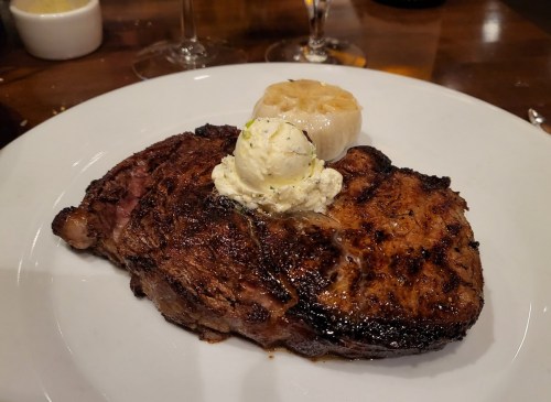 A perfectly cooked steak topped with herb butter and served with a grilled banana on a white plate.