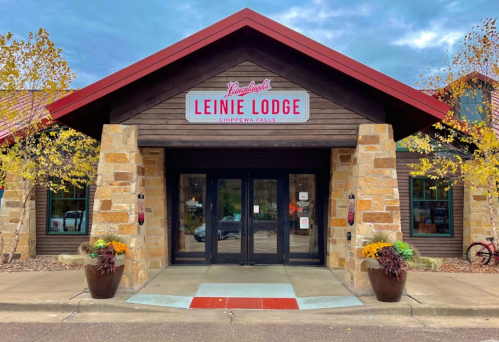 Exterior of Leinie Lodge in Chippewa Falls, featuring a stone facade, red roof, and colorful flower pots.
