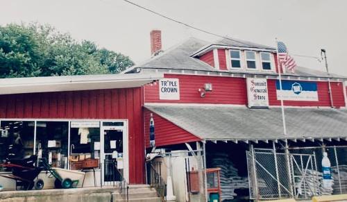 A red general store with a sign reading "Triple Crown," featuring an American flag and various outdoor items visible.