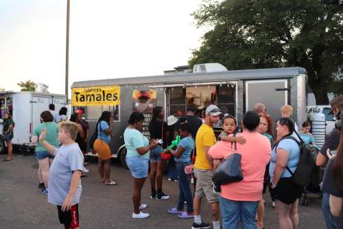 A food truck serving tamales with a crowd of people waiting in line, enjoying a lively outdoor event.