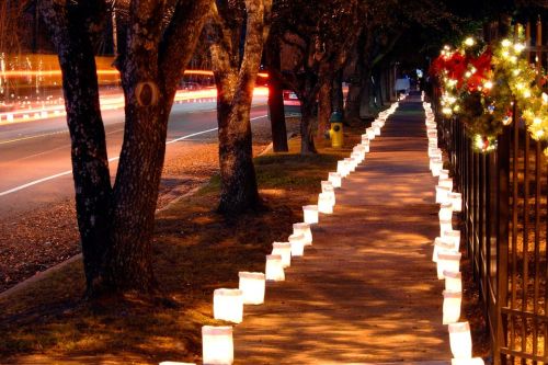A sidewalk lined with glowing lanterns, trees on either side, and festive decorations in the background.