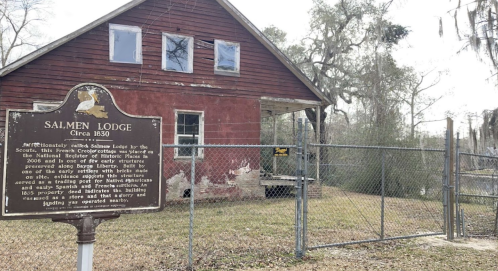 Historic Salmen Lodge, built circa 1830, with a weathered red exterior and a sign marking its historical significance.