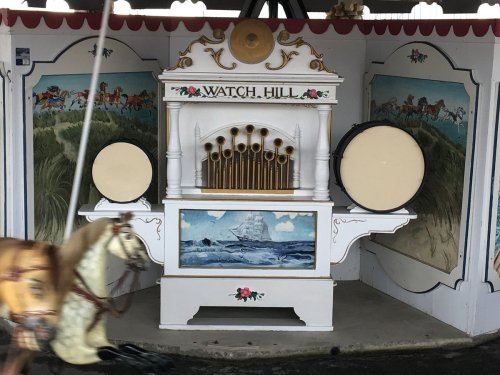 A vintage carousel organ with pipes and drums, decorated with floral designs and scenic murals in the background.