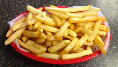 A red basket filled with golden, crispy French fries on a dark countertop.