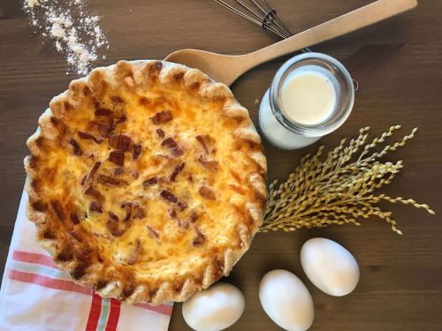 A freshly baked pie with a golden crust, surrounded by eggs, milk, flour, and a wooden spoon on a rustic table.