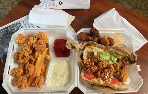 A takeout meal featuring fried shrimp, crinkle-cut fries, dipping sauces, and a shrimp sandwich with lettuce and tomatoes.