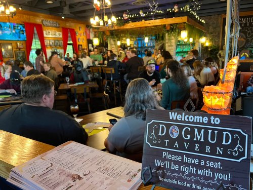 A busy tavern filled with patrons, featuring a welcome sign and cozy decor.