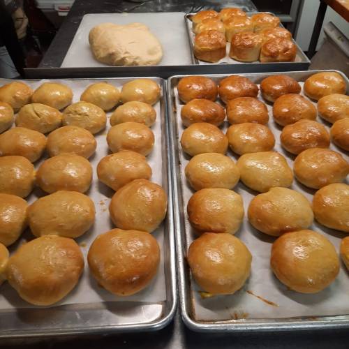Freshly baked golden rolls on trays, with a batch of dough in the background.
