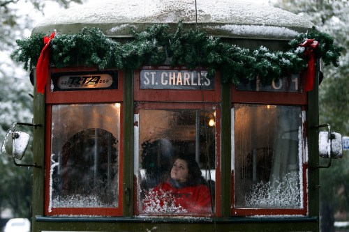 A snow-covered streetcar decorated with greenery, featuring a person gazing out the window.