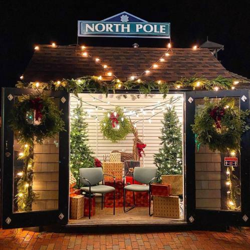 A festive North Pole-themed display with Christmas trees, wreaths, and wrapped gifts, illuminated by string lights.