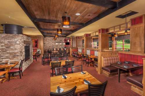 Cozy restaurant interior with wooden tables, chairs, and stone accents, featuring warm lighting and a welcoming atmosphere.