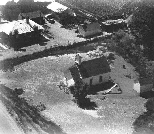 Aerial view of a small town with a church, surrounded by floodwaters and several buildings in the background.