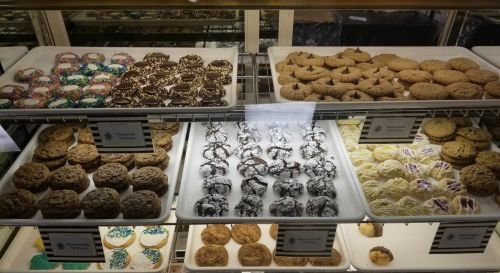 A display case filled with various cookies and pastries, including chocolate-covered treats and colorful frosted cookies.