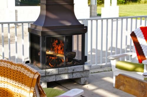 A cozy outdoor fireplace with flames, surrounded by colorful chairs and a sunny patio setting.