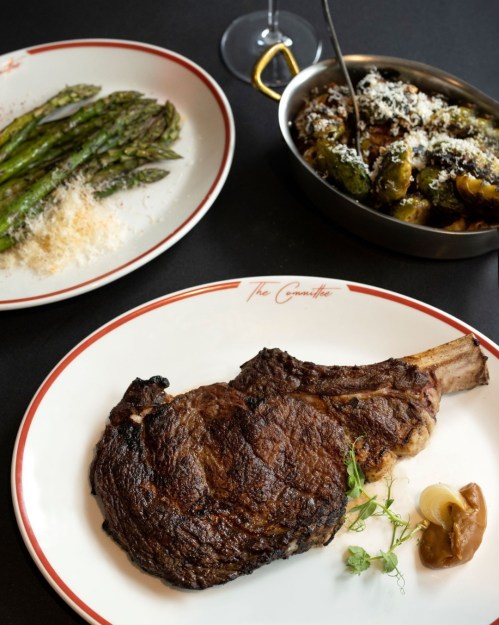 A beautifully plated ribeye steak with sides of asparagus and Brussels sprouts, served on elegant dinnerware.