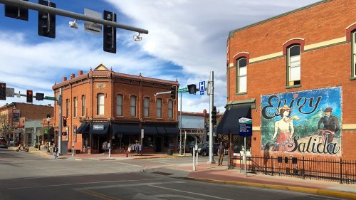 A vibrant street scene featuring historic buildings, traffic lights, and a mural that says "Enjoy Salida."