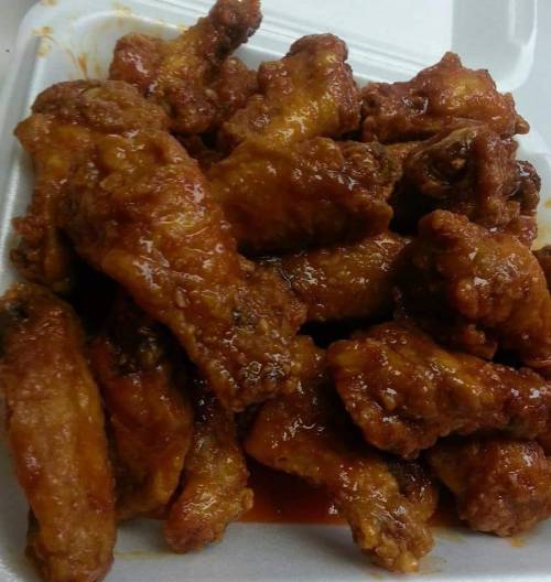 A close-up of crispy, sauced chicken wings piled on a white takeout container.